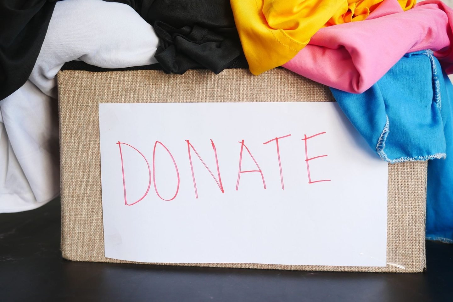 Caixa com a palavra DONATE escrita e roupas coloridas transbordando por cima.