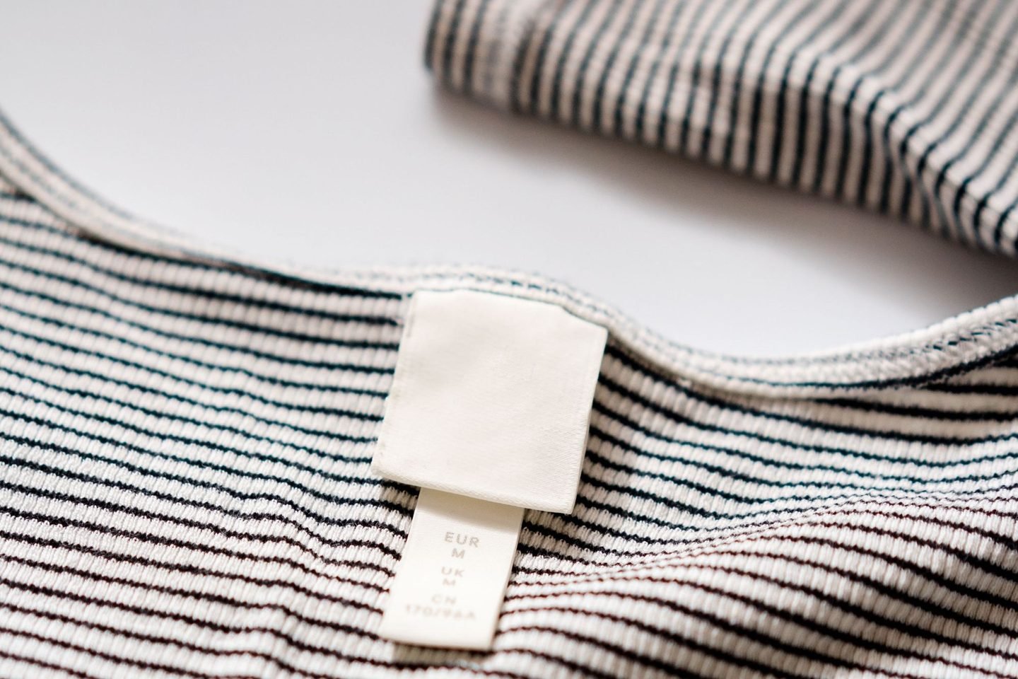 Etiqueta de roupa à mostra na gola de uma camiseta listrada, em close.