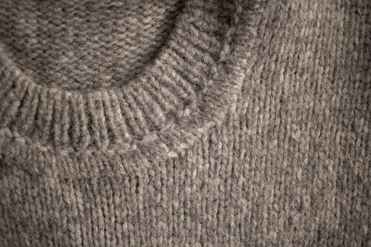 Gola de um suéter de lã cinza em close, com o tricô à mostra.
