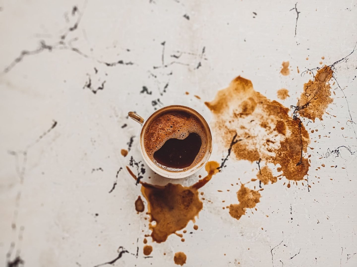 Xícara de café vista de cima, com respingos de café derramados sobre uma superfície de mármore.