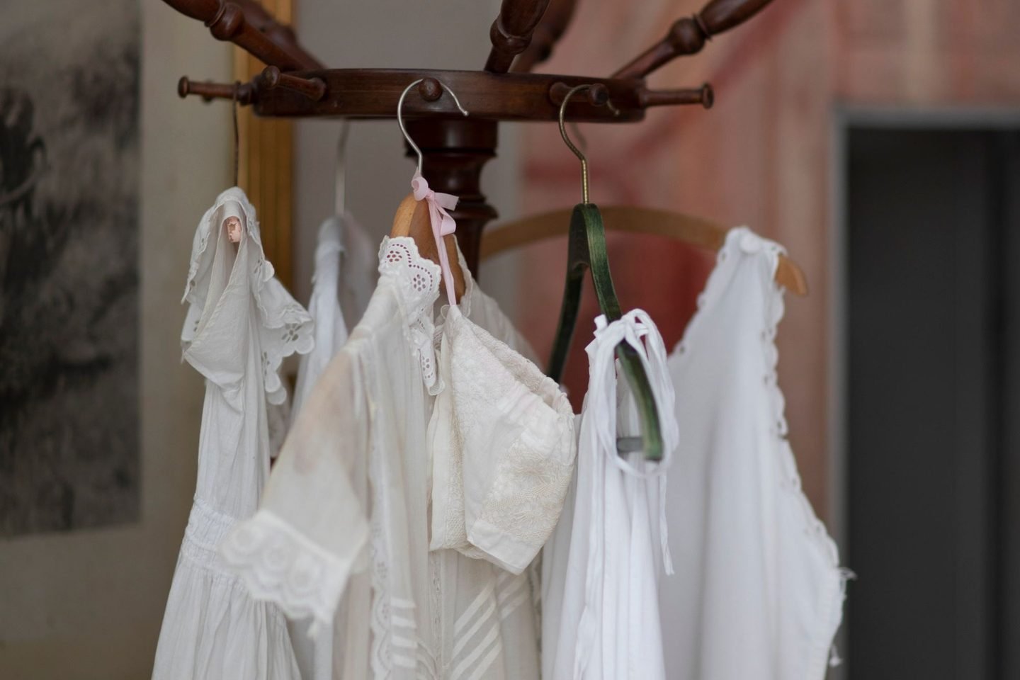 Vestidos brancos antigos pendurados num cabideiro de madeira torneada.