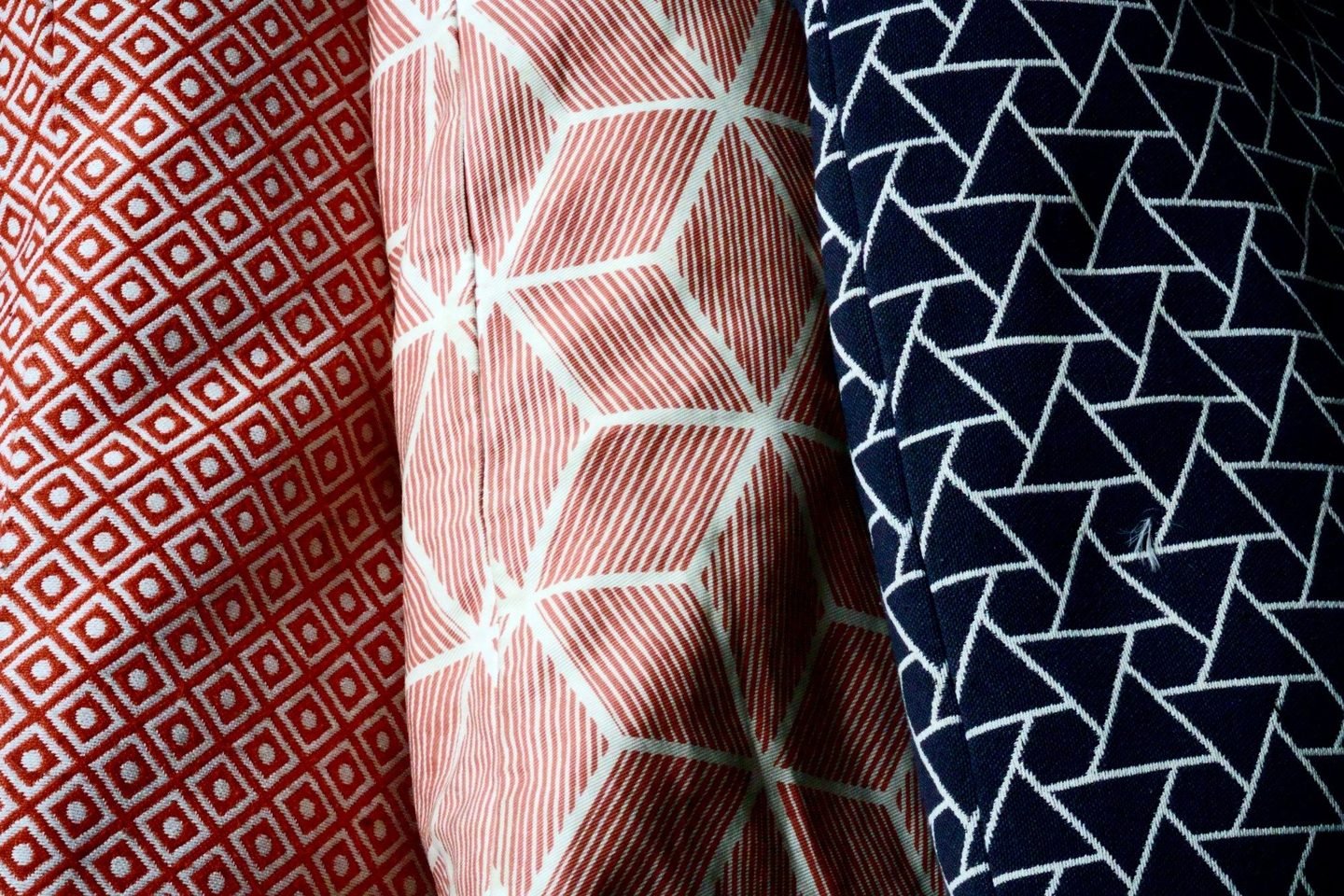 Tecidos com estampas geométricas em vermelho, branco e azul-marinho, em close.