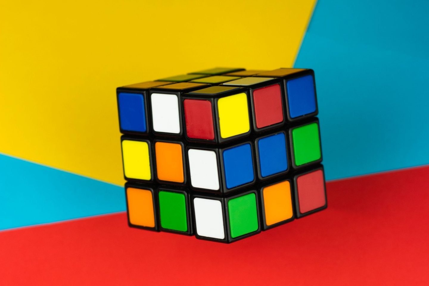 Cubo mágico colorido sobre um fundo dividido em vermelho, amarelo e azul.