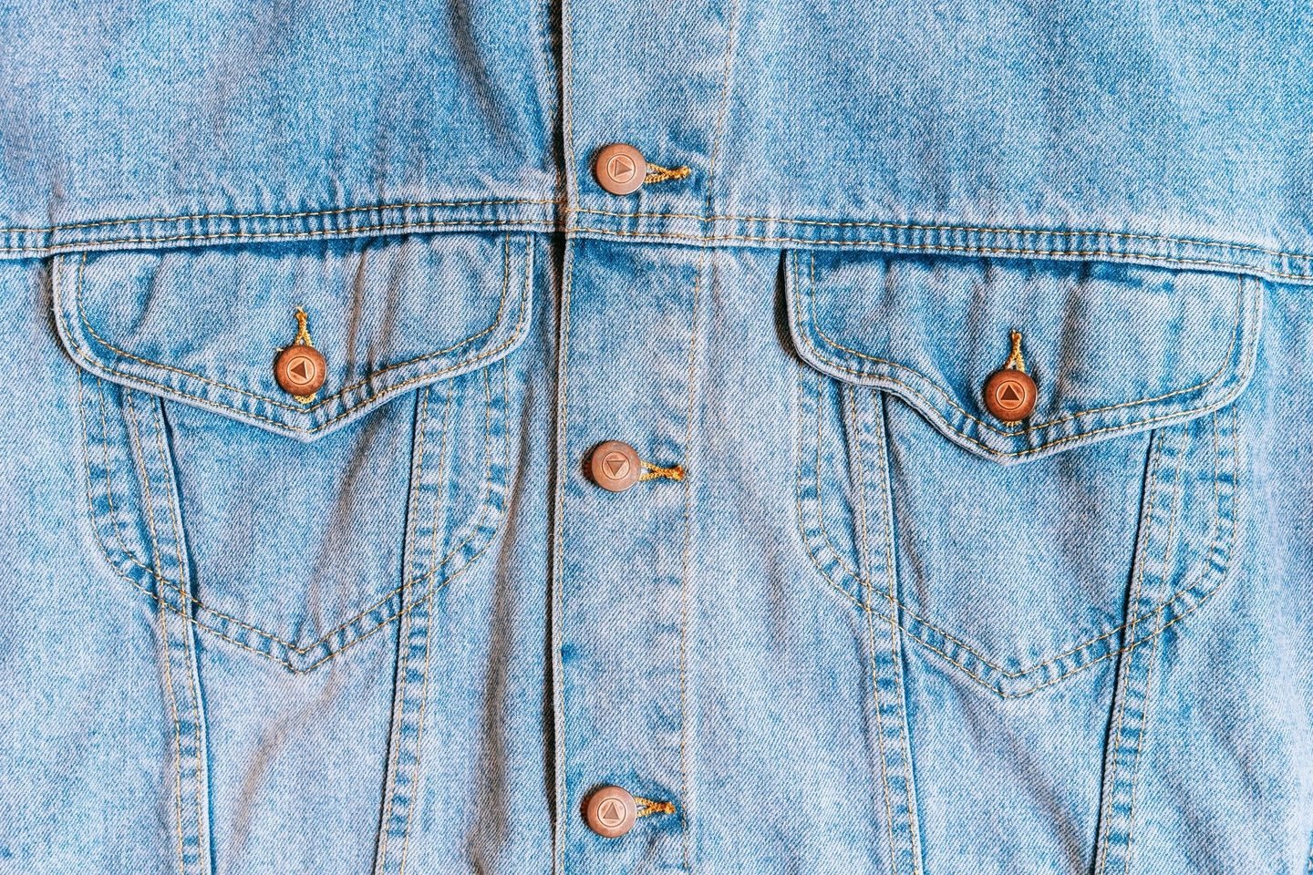 Jaqueta jeans clara em close, com os botões e os bolsos à mostra.