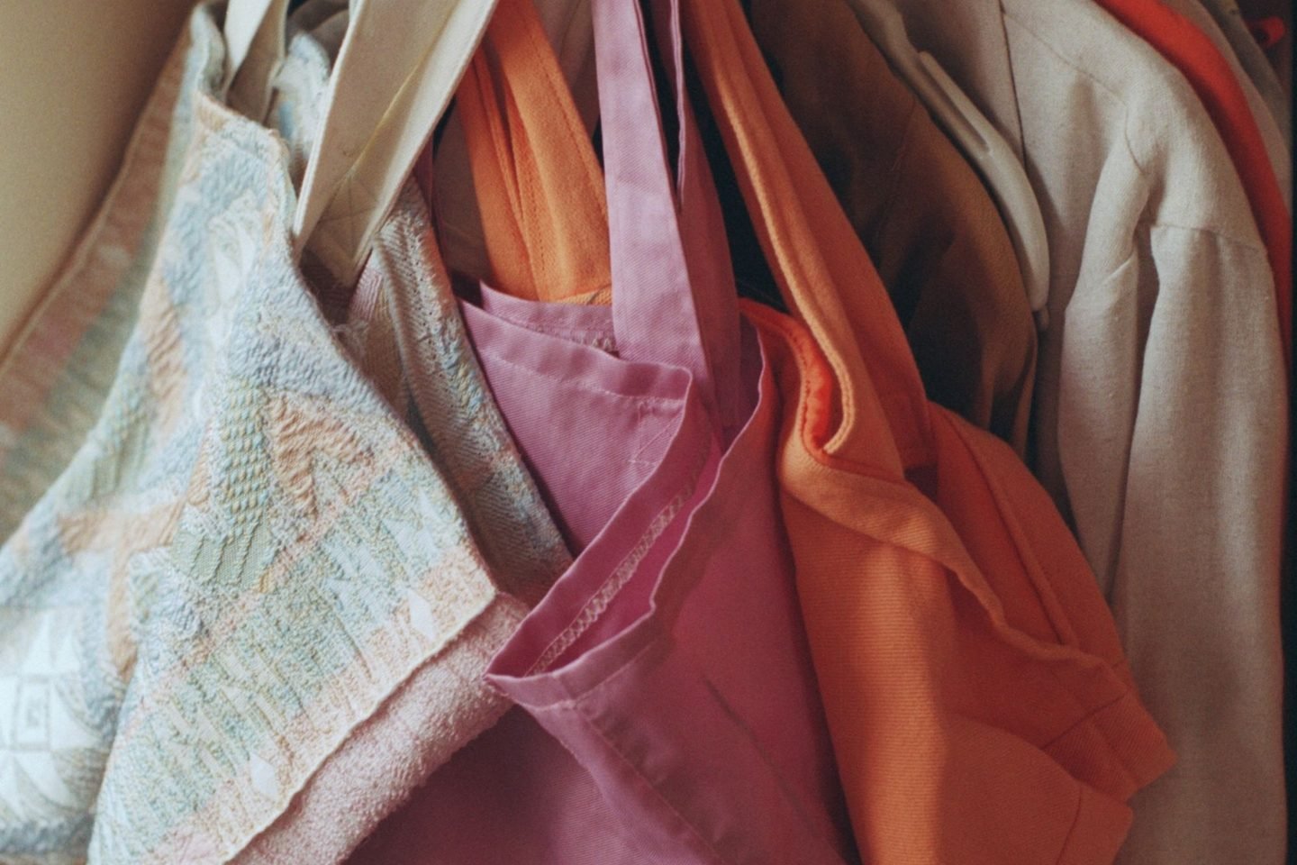 Sacolas de pano e roupas penduradas em cabides numa arara.