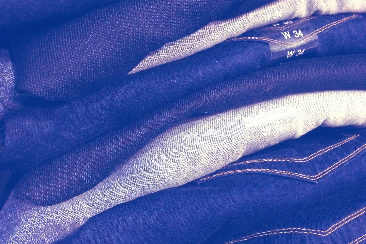 Pilha de calças jeans dobradas, com etiquetas de tamanho nas dobras.