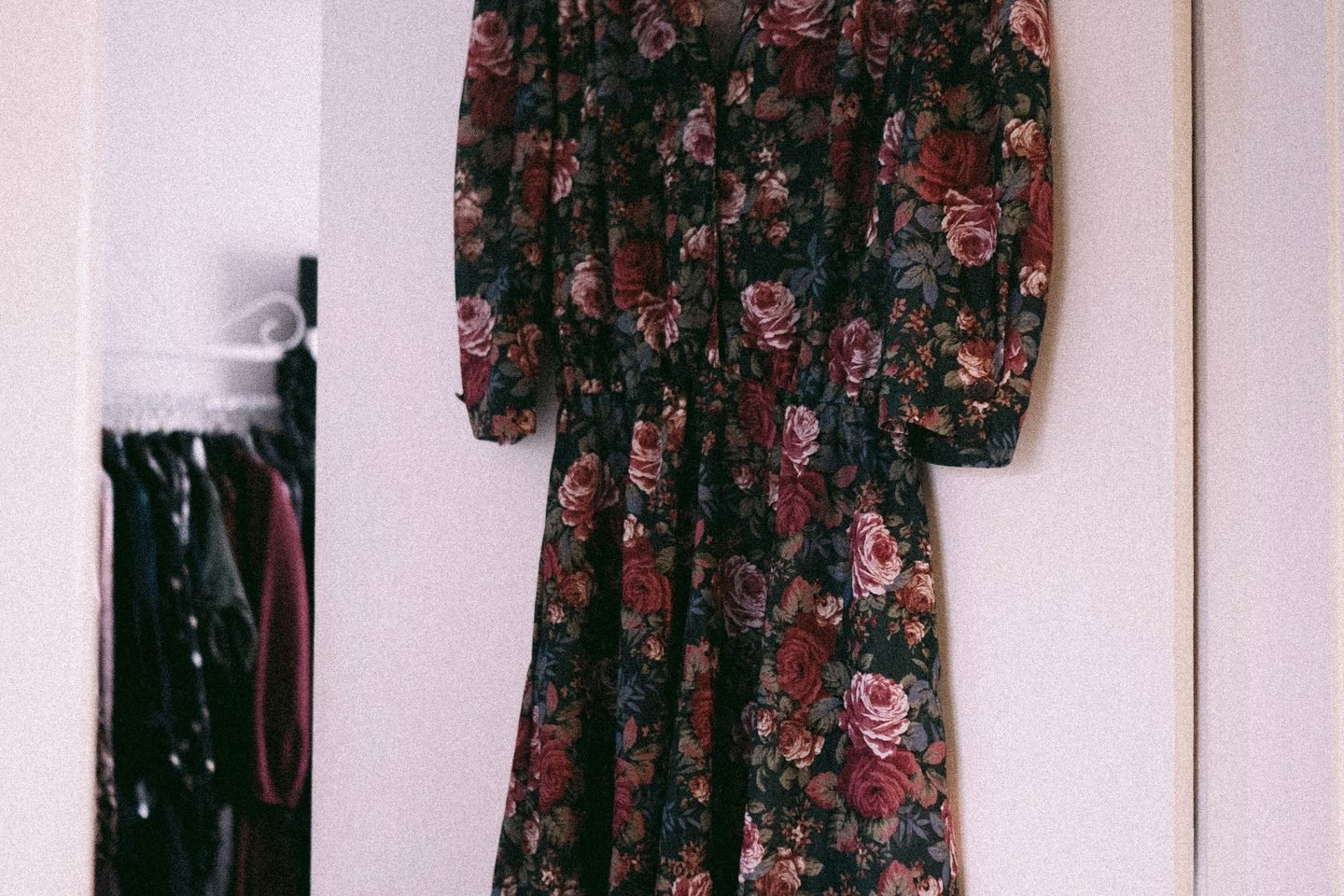 Vestido florido de época pendurado num armário, sob luz suave.